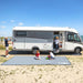 Alfombra Fiamma Patio Mat 440 extendida junto a una autocaravana en la playa, ideal para camping y exteriores