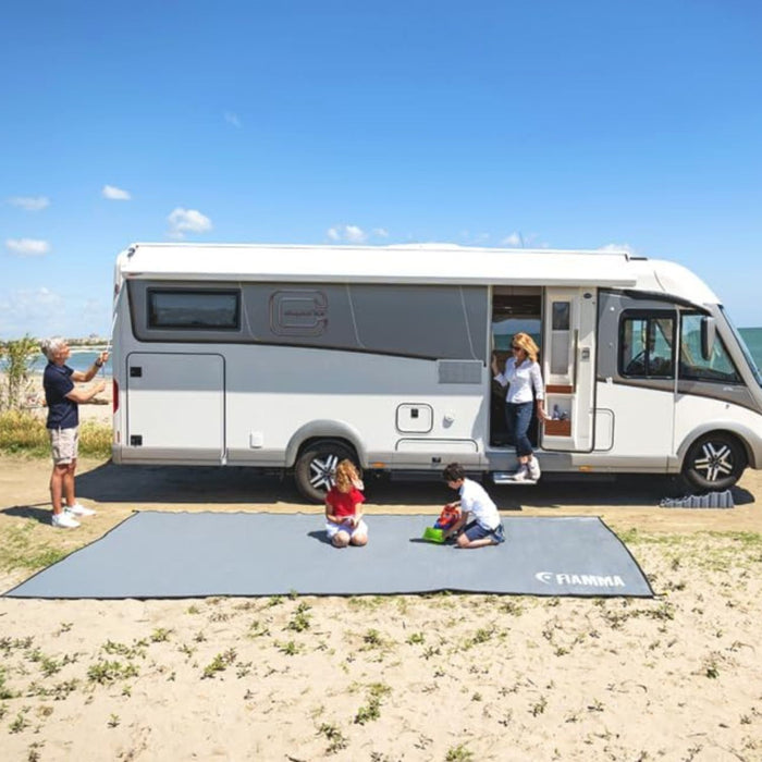 Alfombra Fiamma Patio Mat 490 extendida junto a una autocaravana en la playa, ideal para camping y exteriores